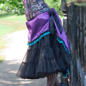 Pu&ograve; includere: Un outfit di ispirazione steampunk con un corsetto viola e nero, una gonna nera a strati e calze a righe. La gonna ha una sopragonna viola con bordi in pizzo turchese. Le scarpe nere con tacco completano il look.