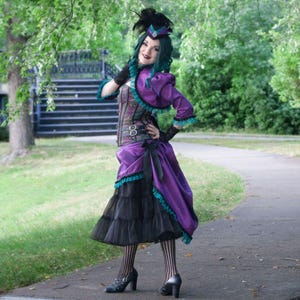Pu&ograve; includere: Un outfit viola e nero di ispirazione steampunk. L'ensemble comprende un corsetto, un bolero e una gonna a strati. Dettagli turchesi rifiniscono i bordi della giacca e della gonna. Un cappello abbinato con piume completa il look. L'outfit &egrave; indossato con calze a righe e scarpe col tacco.