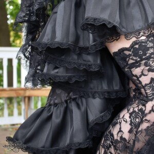 May include: Black layered skirt with ruffled trim and lace overlay. The skirt is made of a silky fabric and has a tiered design.