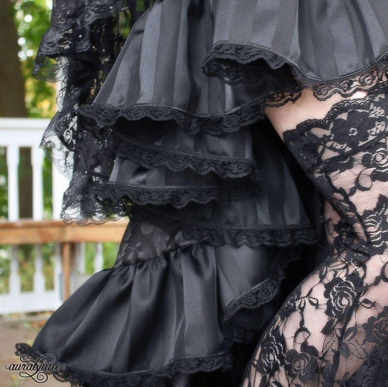 May include: Black layered skirt with ruffled trim and lace overlay. The skirt is made of a silky fabric and has a tiered design.