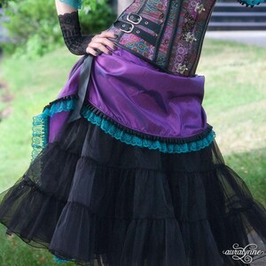 Pu&ograve; includere: Gonna steampunk viola e nera con corsetto abbinato. La gonna presenta strati di tulle nero e una sopragonna viola con bordatura in pizzo turchese. Il corsetto &egrave; un mix di tonalit&agrave; viola, nere e bronzo, con fibbie argentate.