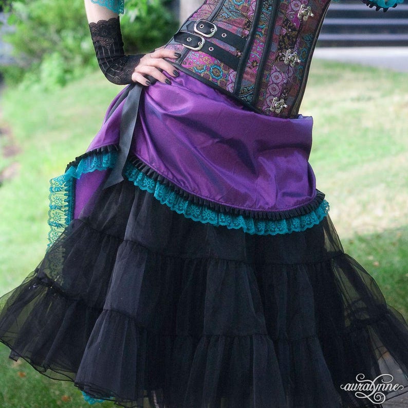 Pu&ograve; includere: Gonna steampunk viola e nera con corsetto abbinato. La gonna presenta strati di tulle nero e una sopragonna viola con bordatura in pizzo turchese. Il corsetto &egrave; un mix di tonalit&agrave; viola, nere e bronzo, con fibbie argentate.