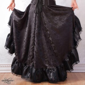 May include: A black satin skirt with a floral pattern and a lace trim. The skirt has a fitted waistband and a flowing, full skirt.