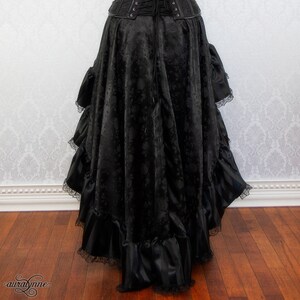 May include: A black maxi skirt with a ruffled hem and a lace trim. The skirt is made of a textured fabric and has a fitted waistband.