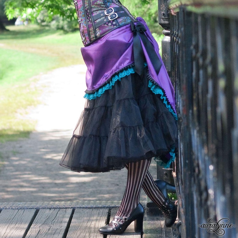 Pu&ograve; includere: Un outfit di ispirazione steampunk con un corsetto viola e nero, una gonna nera a strati e calze a righe. La gonna ha una sopragonna viola con bordi in pizzo turchese. Le scarpe nere con tacco completano il look.