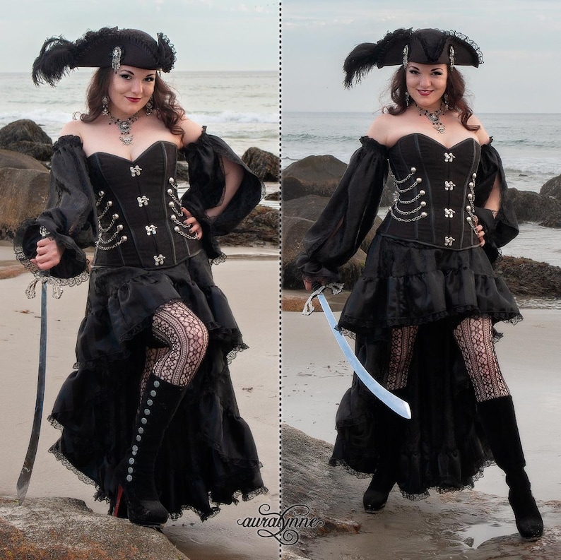 May include: A woman in a black pirate costume with a black corset, a black skirt with ruffles, and black boots. She is holding a sword in each hand and is standing on a beach.