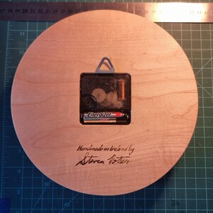 May include: A round wooden clock back with a clock mechanism and an Energizer battery. The text "Handmade in Ireland by Steven Potter" is inscribed on the wood. A metal ruler is visible in the background.