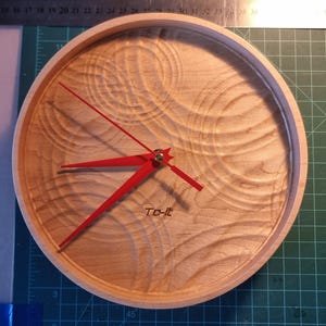 May include: A round wooden clock with a light wood grain finish. The clock features bright red hands and a red second hand. The text "To-it" is printed at the bottom. The clock's diameter is approximately 10 inches.