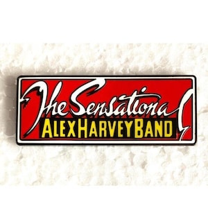 May include: Red and yellow enamel pin with the text "The Sensational Alex Harvey Band".