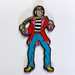 May include: An enamel pin featuring a cartoon character with long black hair, wearing a red jacket, a black and white striped shirt, blue jeans and yellow boots. The character is holding a green whip.