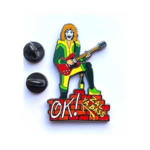 Peut inclure: Une épingle en émail colorée représentant un personnage de dessin animé jouant de la guitare électrique rouge sur un mur de briques avec le texte "OK! Ya'll Bass" en jaune et rouge.