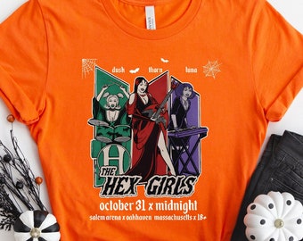 May include: Orange t-shirt with a graphic of three women playing instruments. The graphic is in a retro style and includes the text "The Hex Girls" and "October 31 x Midnight".