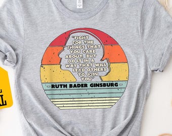 May include: Sport Grey t-shirt featuring a quote by Ruth Bader Ginsburg in a retro design. The quote is inside a circular design with a silhouette of a person's profile. The shirt has a tag with 3XL and 4XL sizes.