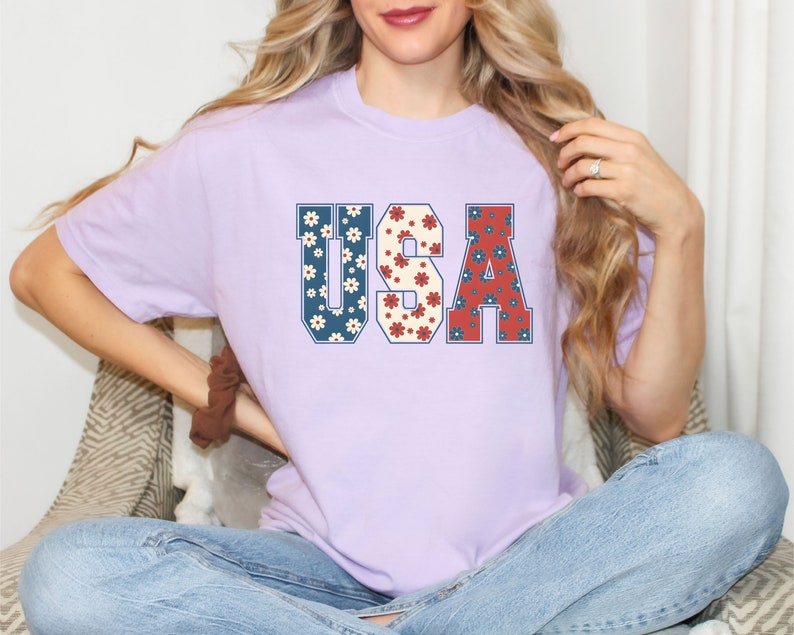 May include: A lavender t-shirt with a graphic of the word "USA" in blue, red, and white with a floral pattern.