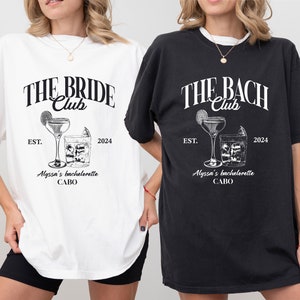 K&ouml;nnte beinhalten: Zwei wei&szlig;e T-Shirts mit schwarzem Text und Grafiken. Der Text auf dem linken Shirt lautet "THE BRIDE Club EST. 2024 Alyssa's bachelorette CABO". Der Text auf dem rechten Shirt lautet "THE BACH Club EST. 2024 Alyssa's bachelorette CABO".