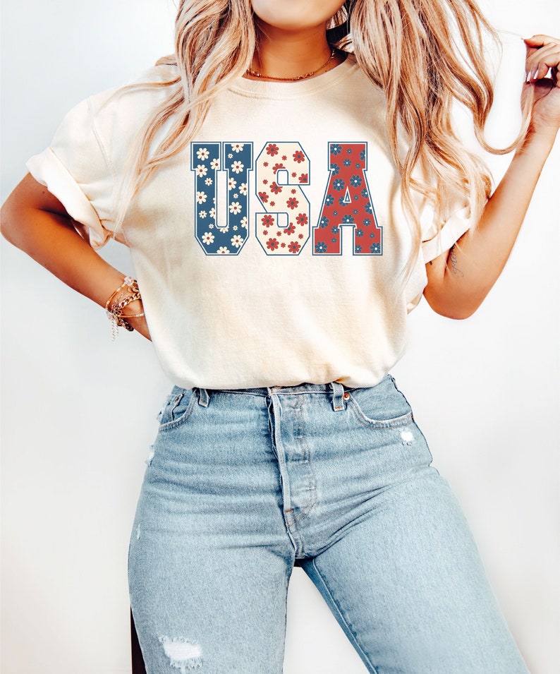 May include: A white t-shirt with a floral patterned graphic of the word "USA" in red, white, and blue.