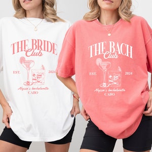 K&ouml;nnte beinhalten: Zwei &uuml;bergro&szlig;e T-Shirts mit einem Junggesellinnenabschied-Motiv. Das wei&szlig;e Shirt sagt "The Bride Club" und das korallenfarbene Shirt sagt "The Bach Club". Beide Shirts zeigen ein Cocktailglas mit einer Limettenscheibe und Eisw&uuml;rfeln. Der Text auf beiden Shirts lautet "Est. 2024" und "Alyssa's Bachelorette Cabo".