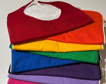 May include: A stack of seven colorful baby bibs with a white terry cloth lining. The bibs are red, orange, yellow, green, blue, purple, and pink.