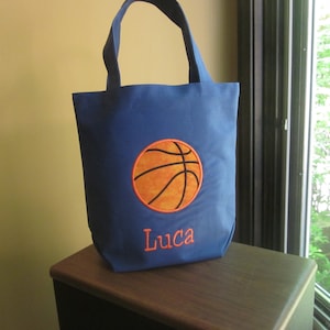 May include: Blue canvas tote bag with an orange basketball and the name Luca embroidered on the front.