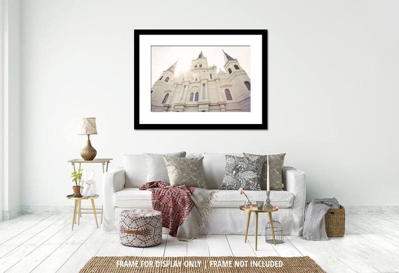 Puede incluir: Una impresi&oacute;n enmarcada de un edificio blanco con m&uacute;ltiples agujas y una torre del reloj. La imagen est&aacute; enmarcada en un marco negro y cuelga sobre un sof&aacute; blanco con cojines decorativos y una otomana estampada. Una peque&ntilde;a mesa auxiliar con una l&aacute;mpara y una planta est&aacute; al lado del sof&aacute;.