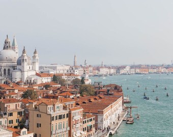 May include: An aerial view of Venice, Italy, with the Basilica di San Giorgio Maggiore in the foreground and the Grand Canal in the background. The city is a maze of narrow canals and bridges, with colorful buildings lining the waterways. The water is a deep blue, and the sky is a clear blue.