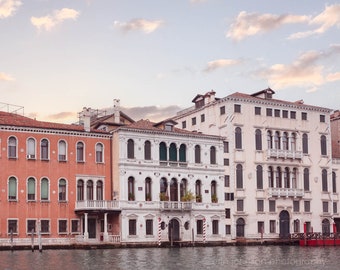 May include: A scenic view of buildings along a canal in Venice, Italy. The buildings feature a variety of architectural styles, with red-tiled roofs, arched windows, and ornate facades. The water reflects the buildings and the sky.