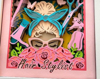 May include: A papercraft framed artwork featuring a stylized illustration of a woman with a blue headband and pink roses. The text "Hair Stylist" is written below the image.