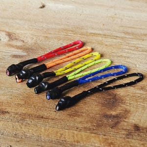 Könnte beinhalten: Ein Set mit sechs bunten Reißverschluss-Zierbändern mit schwarzen Spitzen. Die Bänder sind aus reflektierendem Material und in den Farben Rot, Orange, Gelb, Grün, Blau und Schwarz erhältlich.