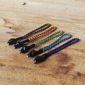 Puede incluir: Cinco tiradores de cremallera con cordón negro y tejido estampado de colores. Los colores son marrón, naranja, verde, azul y morado.