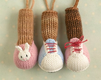 Könnte beinhalten: Drei gestrickte Spielzeugschuhe mit verschiedenen Designs. Der erste Schuh ist rosa mit einem weißen Hasengesicht. Der zweite Schuh ist blau und weiß mit roten Schnürsenkeln. Der dritte Schuh ist rosa und weiß mit roten Schnürsenkeln.