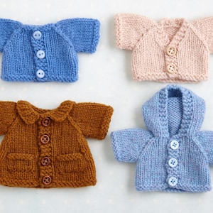 Könnte beinhalten: Vier Miniatur-Strickpullover in verschiedenen Farben: Blau, Rosa und Braun. Der blaue Pullover hat eine Kapuze, während die anderen Kragen oder einen V-Ausschnitt haben. Jeder Pullover hat Knopfverschlüsse, die die Handarbeit hervorheben.