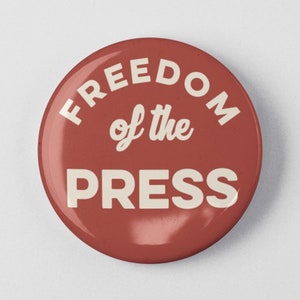 May include: A red button with the text "FREEDOM of the PRESS" in white.