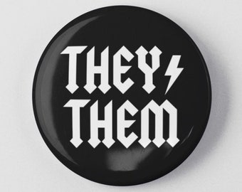 Peut inclure: Bouton noir avec du texte blanc qui dit "THEY/THEM" dans une police gothique audacieuse. Un symbole d'éclair est à côté du mot "THEY".