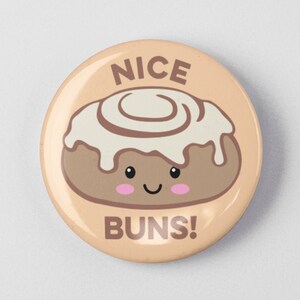 May include: A round button with a cartoon cinnamon roll with icing and a smiling face. The text "NICE BUNS!" is printed below the cinnamon roll.
