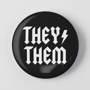 May include: Black button with white text that reads "THEY/THEM" in a bold, gothic font. A lightning bolt symbol is next to the word "THEY".