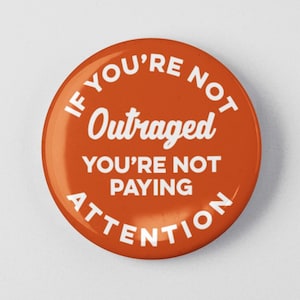May include: Orange button with white text that reads "If you're not outraged you're not paying attention".