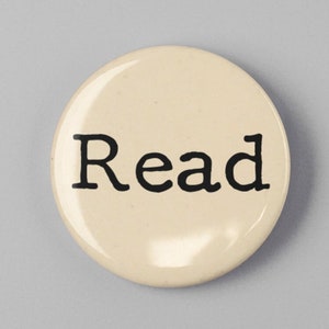 May include: A round, off-white button with the word "Read" printed in black, centered on the face. The button is set against a light gray background, creating a simple, clean design.