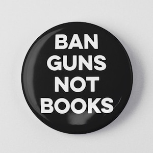 May include: Black button with white text that reads "BAN GUNS NOT BOOKS".
