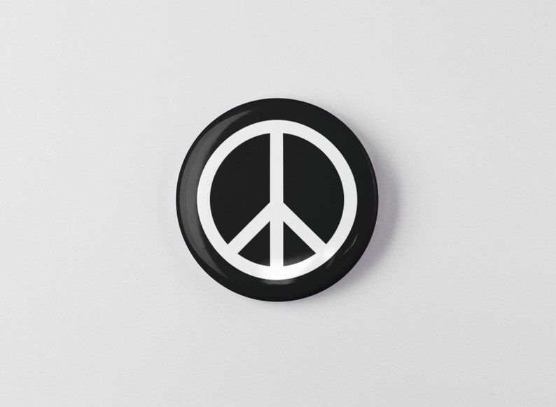 May include: A black and white peace sign button. The peace sign is white and is centered on a black circle.