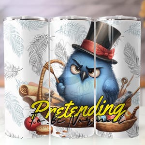 Pode incluir: Um copo branco com um design extravagante com um pássaro azul usando uma cartola e segurando uma cesta. O pássaro tem uma expressão zangada. O copo tem as palavras "Pretending to be normal" em letras amarelas.