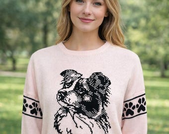 May include: A light pink sweater featuring a black and white dog graphic on the front. The sleeves have black bands with paw print designs. The sweater is made of a soft knit material.