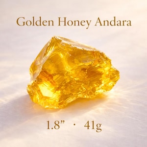 May include: A golden honey Andara crystal, approximately 1.8 inches in size and weighing 41 grams. The crystal has a rough, irregular shape and a translucent, honey-like color. The text "Golden Honey Andara" is displayed above the crystal.