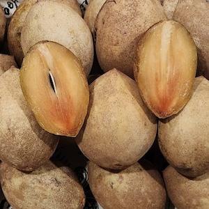 May include: Close-up of a group of brown sapodilla fruits, some cut open to reveal their light brown flesh.