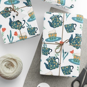 May include: White gift wrap with a repeating pattern of blue teapots, teacups, and saucers with yellow flowers. The teacups and saucers have a blue and white border. The teapots have a green handle and spout. The background is white with green leaves and red flowers.