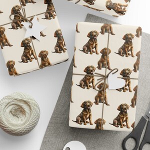 May include: A sheet of wrapping paper with a repeating pattern of brown Labrador Retriever puppies. The paper is cream colored with a subtle texture. The puppies are depicted in a realistic style with brown fur and black noses.