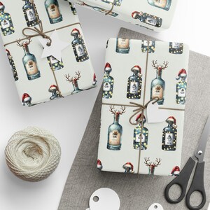 May include: White wrapping paper with a repeating pattern of illustrated bottles of gin with a reindeer head and a Santa hat. The bottles are decorated with lights and the word "GIN" is printed on the label. The paper is tied with twine and a star-shaped tag.