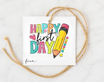 May include: A square white tag with the words "HAPPY first DAY" in colourful letters and a yellow pencil illustration. The tag is tied with a brown twine string, ideal for back-to-school gifts.