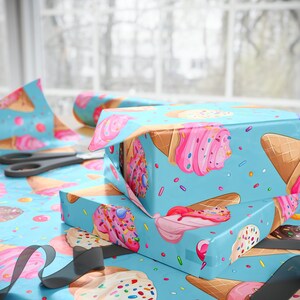 May include: Two gift boxes wrapped in blue wrapping paper with a pattern of ice cream cones and sprinkles. The boxes are stacked on top of each other and are tied with a black ribbon.