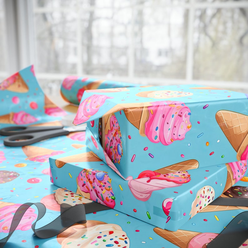May include: Two gift boxes wrapped in blue wrapping paper with a pattern of ice cream cones and sprinkles. The boxes are stacked on top of each other and are tied with a black ribbon.