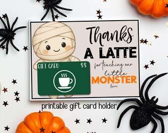 May include: A Halloween-themed gift card holder with a mummy illustration and the text "Thanks a Latte for teaching our little Monster." A green gift card with a coffee cup icon is included. Decorative spiders, stars, and pumpkins surround the card.